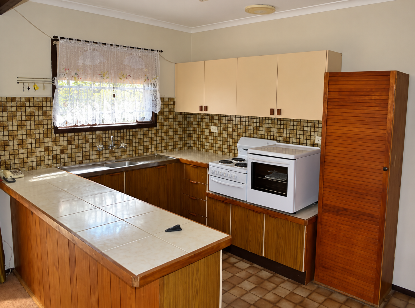 Old kitchen with tiled benchtops, timber cabinets and a freestanding stove before renovation