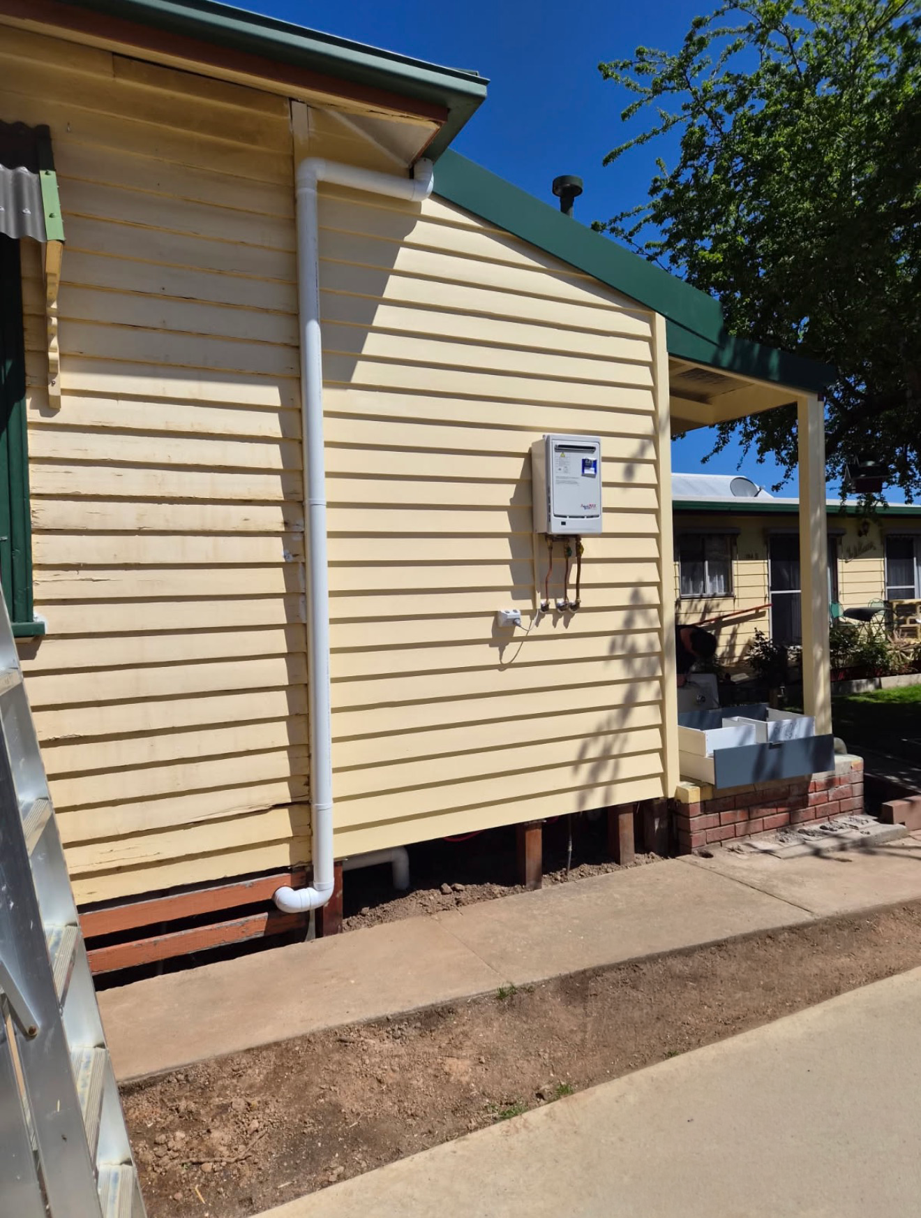 Weatherboard house side after repairs with new downpipes and a gas hot water unit