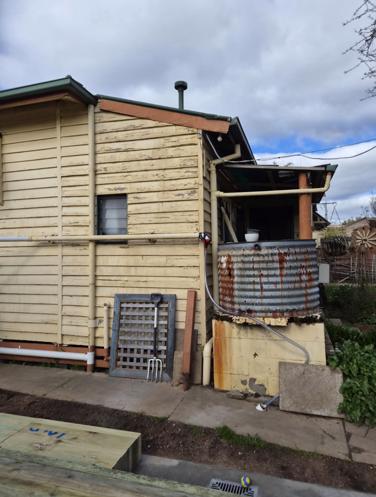 Weatherboard house side with a rusty rainwater tank and worn cladding before repairs